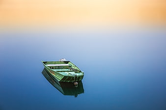 Solitary green boat floating on calm blue water at sunset