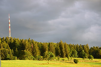 Dramatic landscape with forest, meadow, and radio tower under storm clouds