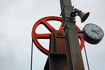 Red ship wheel and clock on metal pole against sky