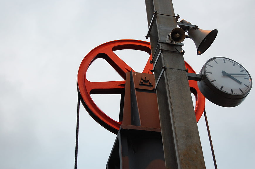 Red ship wheel and clock on metal pole against sky