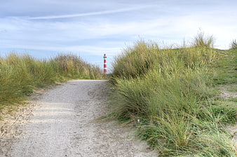 Sandy path through dunes leading to red and white lighthouse