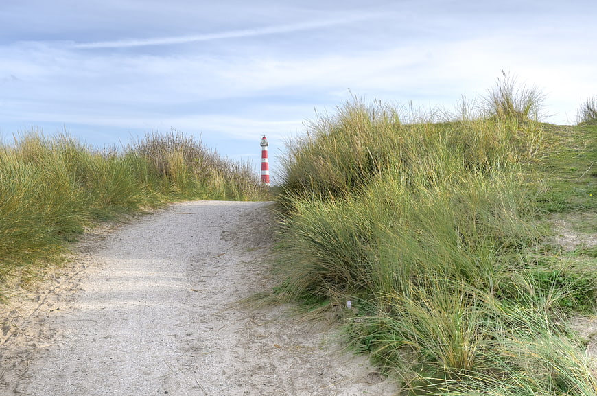 Sandy path through dunes leading to red and white lighthouse