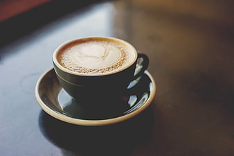Cappuccino with heart latte art in a dark ceramic cup on a wooden table