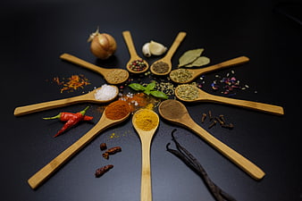 Wooden spoons with assorted spices and herbs arranged on dark background
