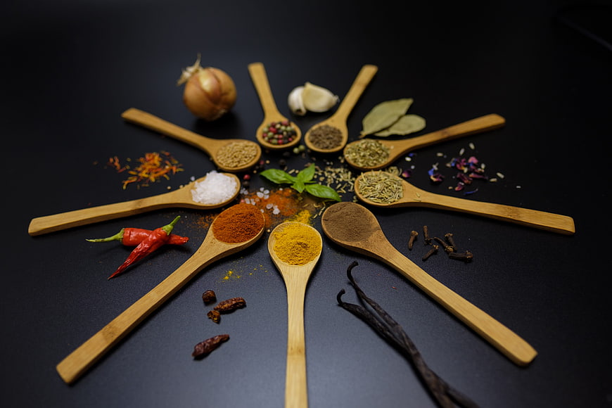 Wooden spoons with assorted spices and herbs arranged on dark background