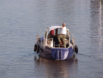 Man steering blue cabin cruiser boat on calm river