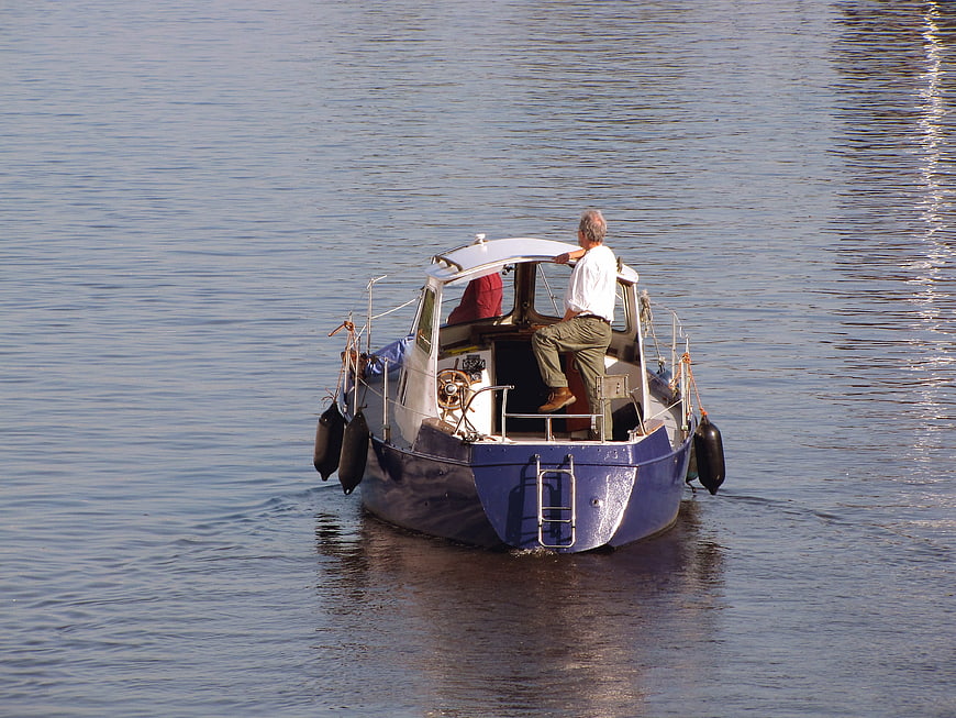 Man steering blue cabin cruiser boat on calm river