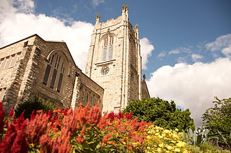 Historic stone church tower with vibrant red and yellow flowers