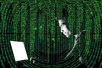 Hacker typing on laptop with green binary code background