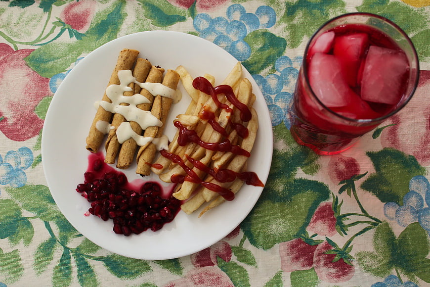 Flat lay of savory rolls, fries, pomegranate, and red juice