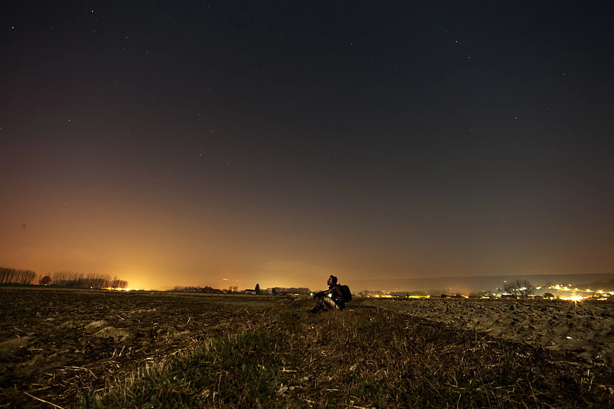 Man Sitting in Field Under Starry Night Sky