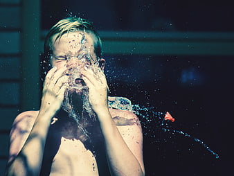 Boy splashing water on face in summer sunlight