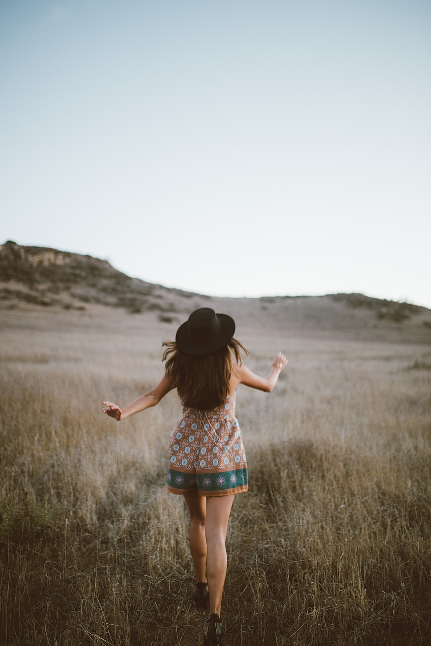 Woman in Hat Running Through Dry Grassland Field