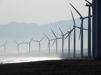 Coastal wind farm turbines silhouetted against hazy mountains and ocean