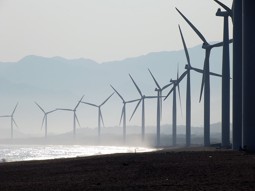 Coastal wind farm turbines silhouetted against hazy mountains and ocean