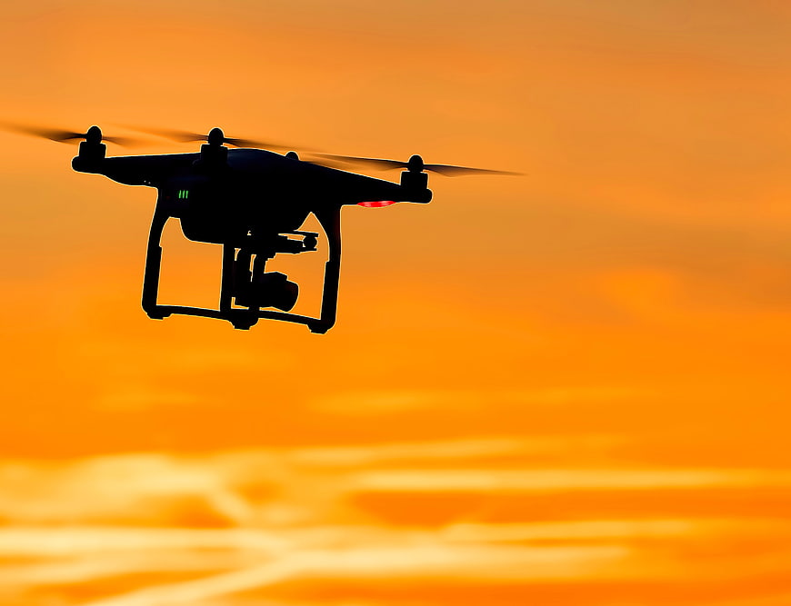 Silhouette of Drone Flying Against Vibrant Orange Sunset Sky