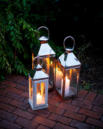 Three lit lanterns on brick path at dusk