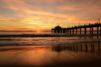 Silhouetted pier at sunset with golden sky and ocean waves