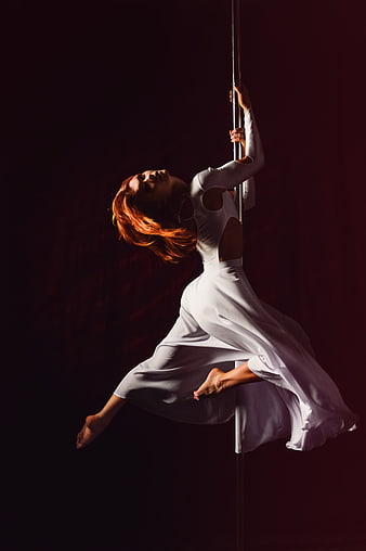 Elegant woman performing pole dance in white dress