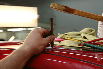 Hand applying black pinstripe to red car in workshop