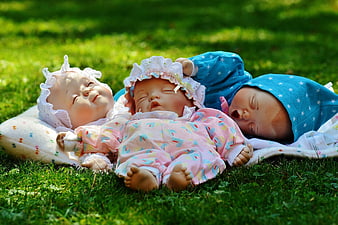 Three sleeping baby dolls lying on green grass