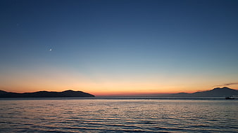 Serene Sea Sunset With Crescent Moon And Distant Mountains