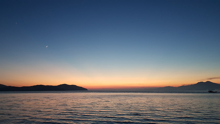 Serene Sea Sunset With Crescent Moon And Distant Mountains