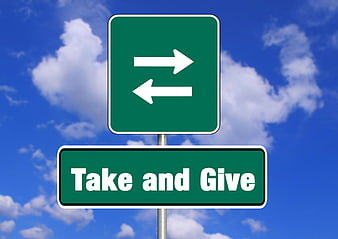 Green Traffic Sign With Take And Give Text Against Blue Sky