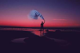 Silhouette of man releasing smoke on beach at sunset