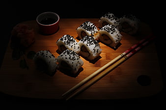 Dark moody sushi rolls with sesame seeds and chopsticks on wooden board