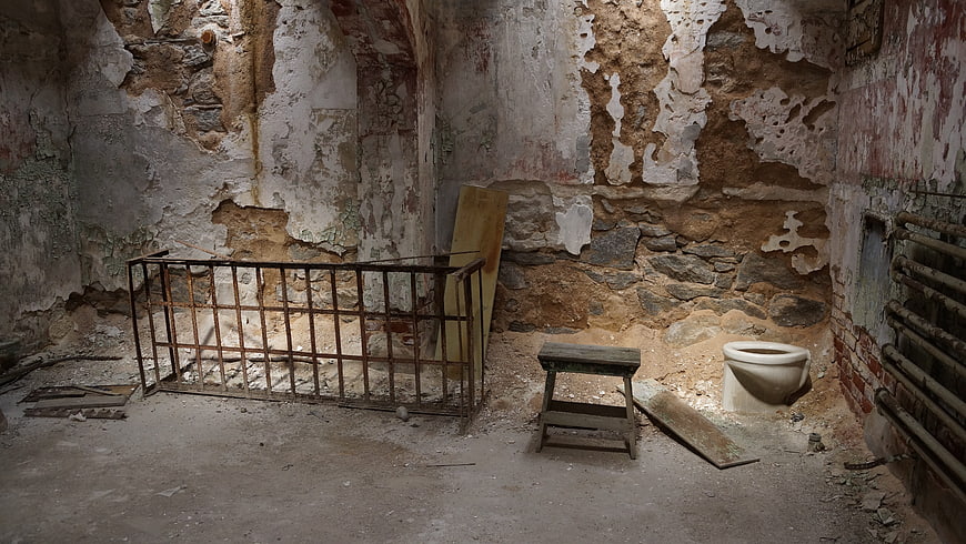 Derelict Prison Cell Interior with Rusty Bed Frame and Toilet