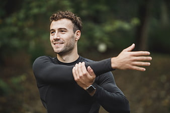 Smiling man stretching arm outdoors in black sportswear