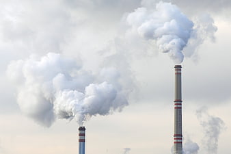Industrial smokestacks emitting white steam against cloudy sky