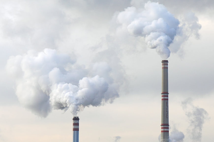Industrial smokestacks emitting white steam against cloudy sky