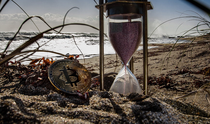 Bitcoin coin and hourglass on a sandy beach with ocean waves