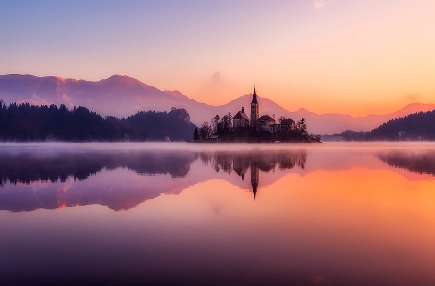Serene Lake Bled Sunrise with Church Reflection and Misty Mountains