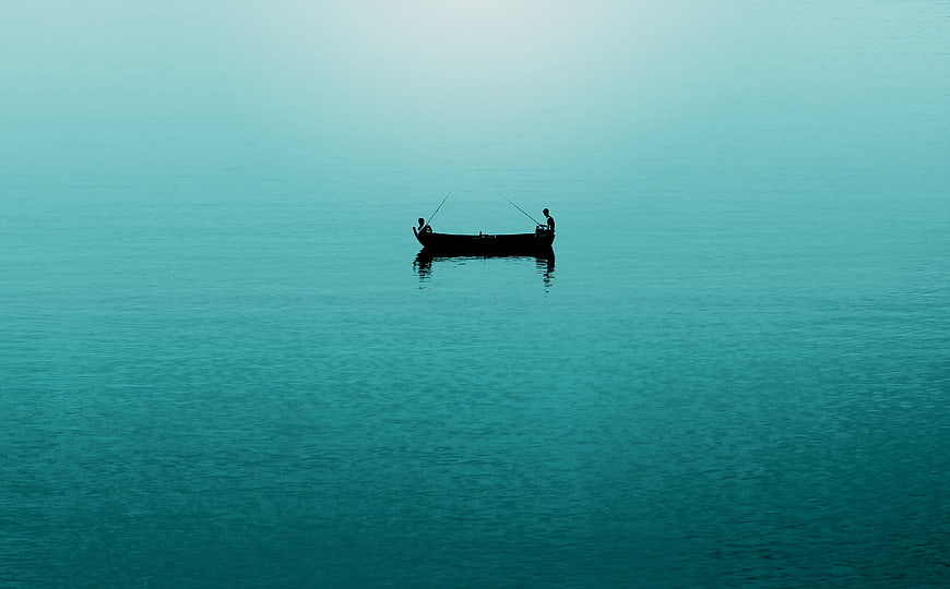 Silhouette of two fishermen in a boat on calm teal water
