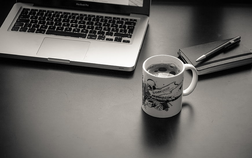 Black and white workspace with laptop, coffee mug, and notebook
