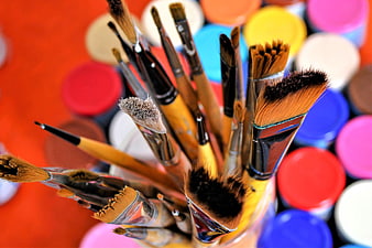 Close-up of colorful paintbrushes in a jar with blurred paint cans