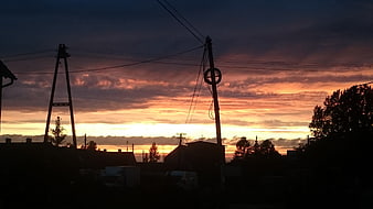 Dramatic sunset silhouette of power lines and rural rooftops