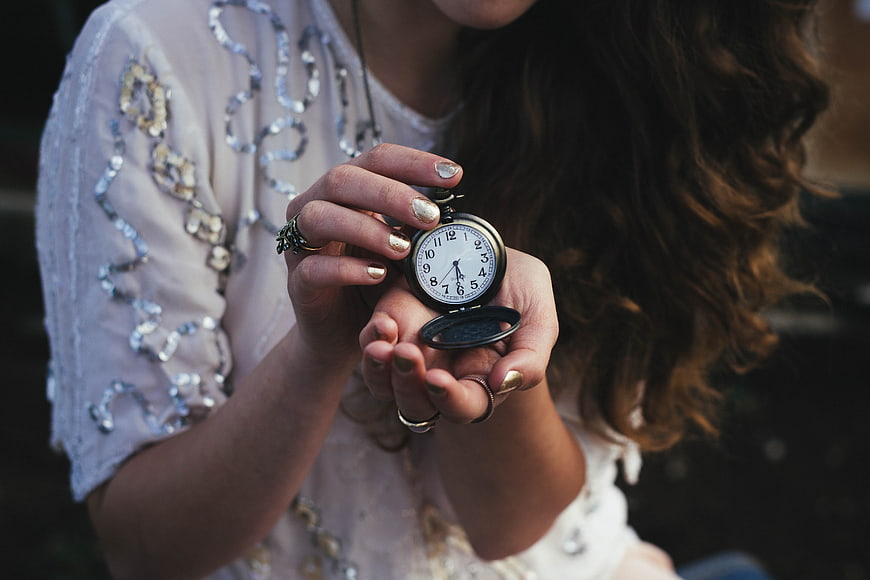 Woman holding vintage pocket watch with gold manicure