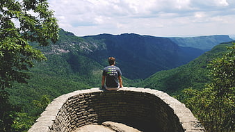 Man Sitting on Stone Wall Overlooking Mountain Valley