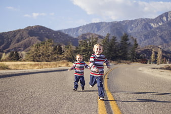 Two young boys running hand in hand on a country road