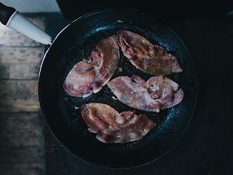 Raw meat slices frying in a cast iron skillet
