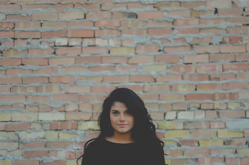 Portrait of young woman with dark hair against brick wall