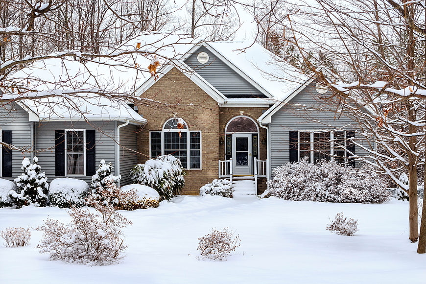 Snow-Covered Gray House with Brick Accents in Winter