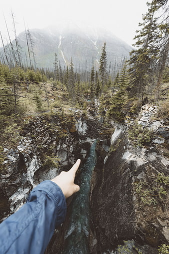 Hand pointing at deep mountain gorge with river
