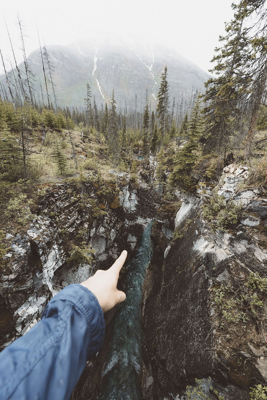 Hand pointing at deep mountain gorge with river