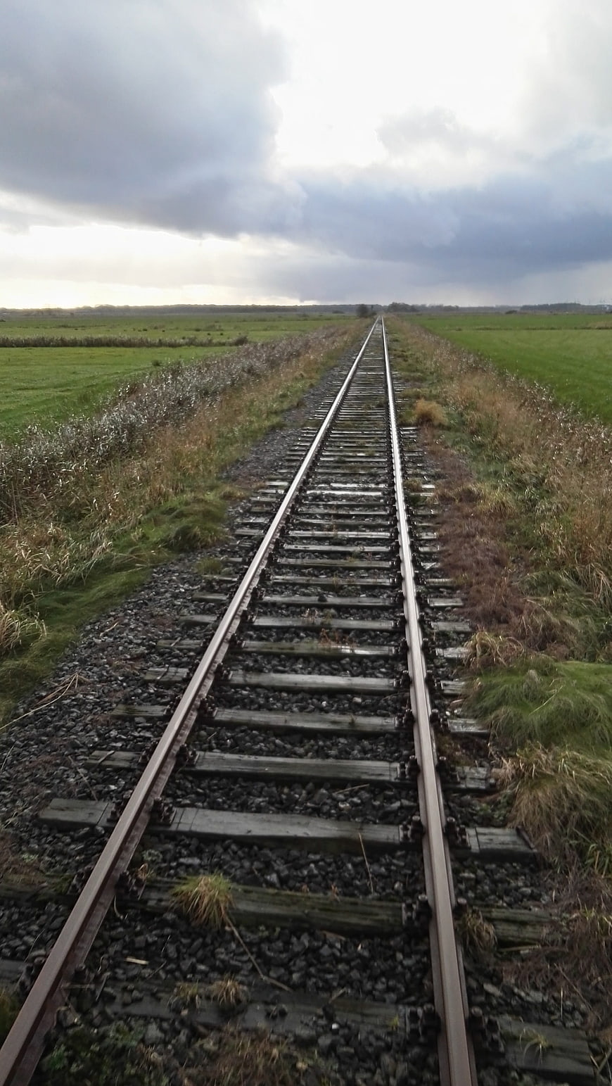 Railway tracks stretching through green countryside under cloudy sky