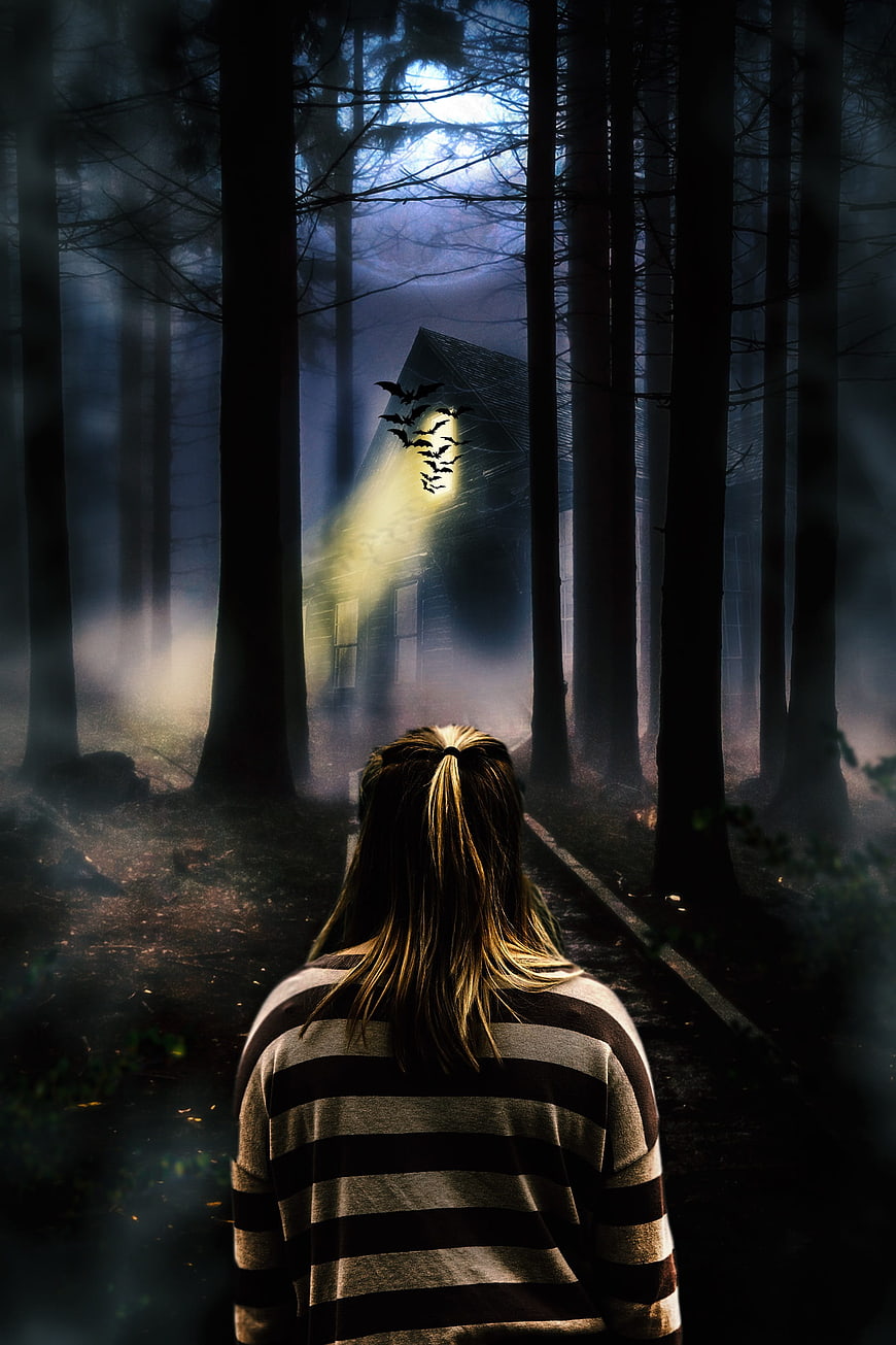 Woman walking toward haunted house in dark forest